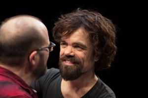 A dramatic close-up profile shot showing curly hair and a beard against a dark background.