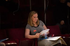 Several people seated in red theater-style chairs reviewing papers or scripts.