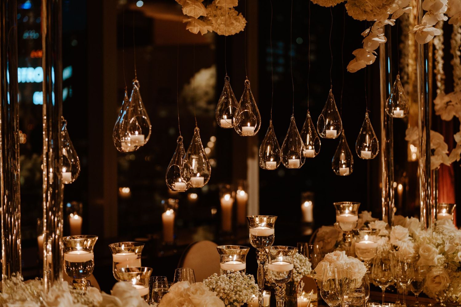 Elegant wedding reception decor with hanging crystal votives and white floral arrangements.