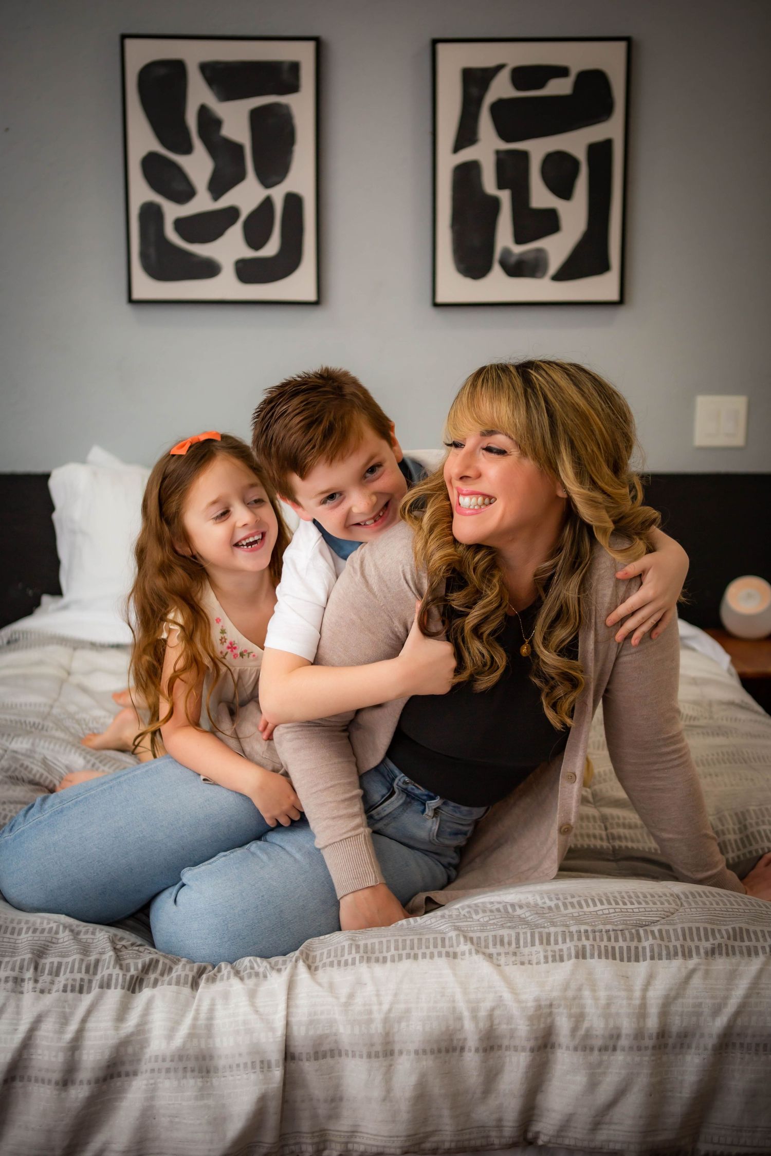 Family shares joyful moment together on bed with modern artwork in background.