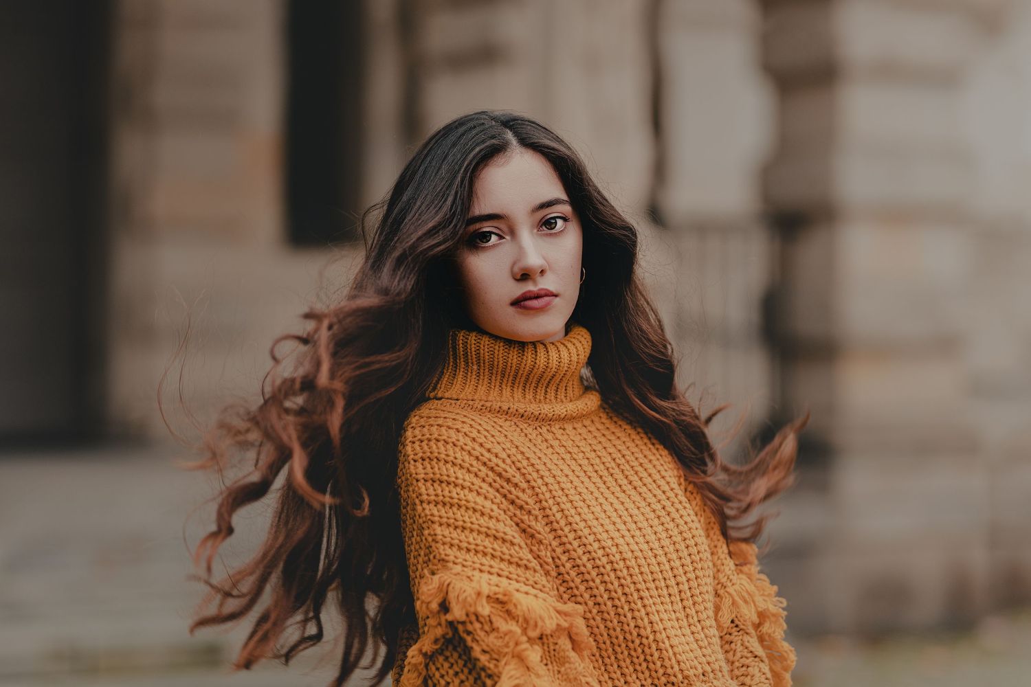 A portrait featuring a mustard yellow knit sweater against stone architecture.