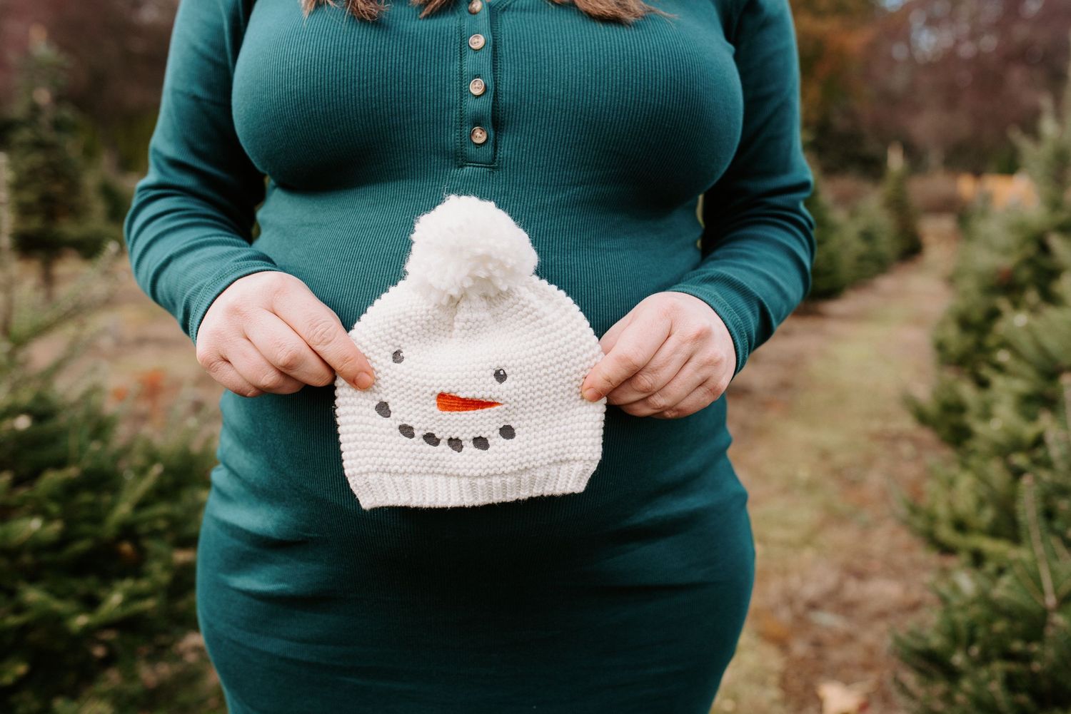 Person in teal sweater holding small white paper snowman cutouts against natural backdrop.
