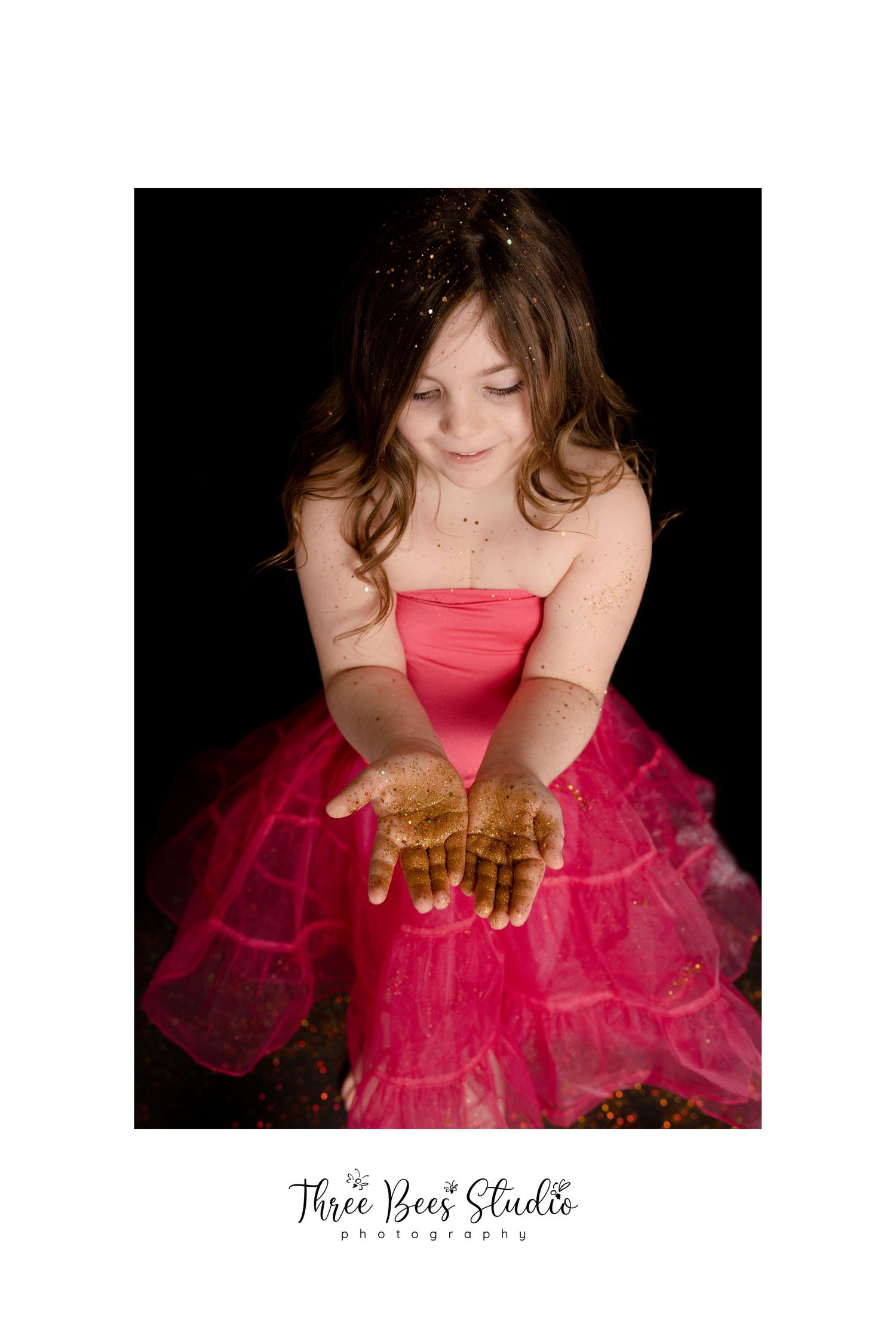 Young person in bright pink tulle dress holding gold glitter against black background.