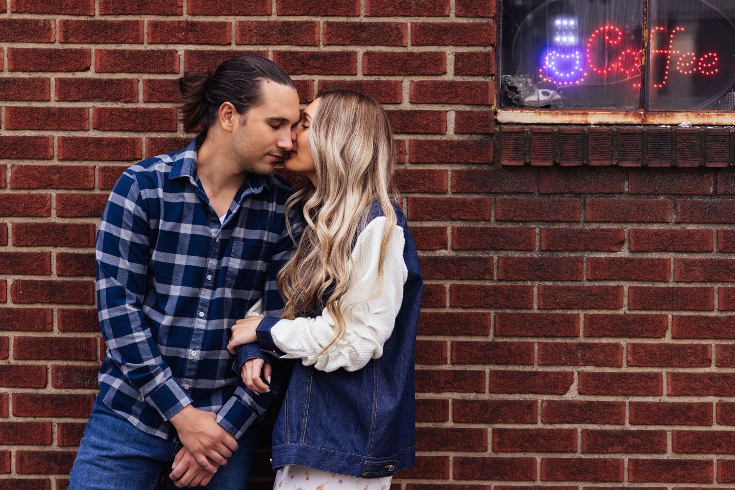 young couple kiss by red brick wall and coffee sign