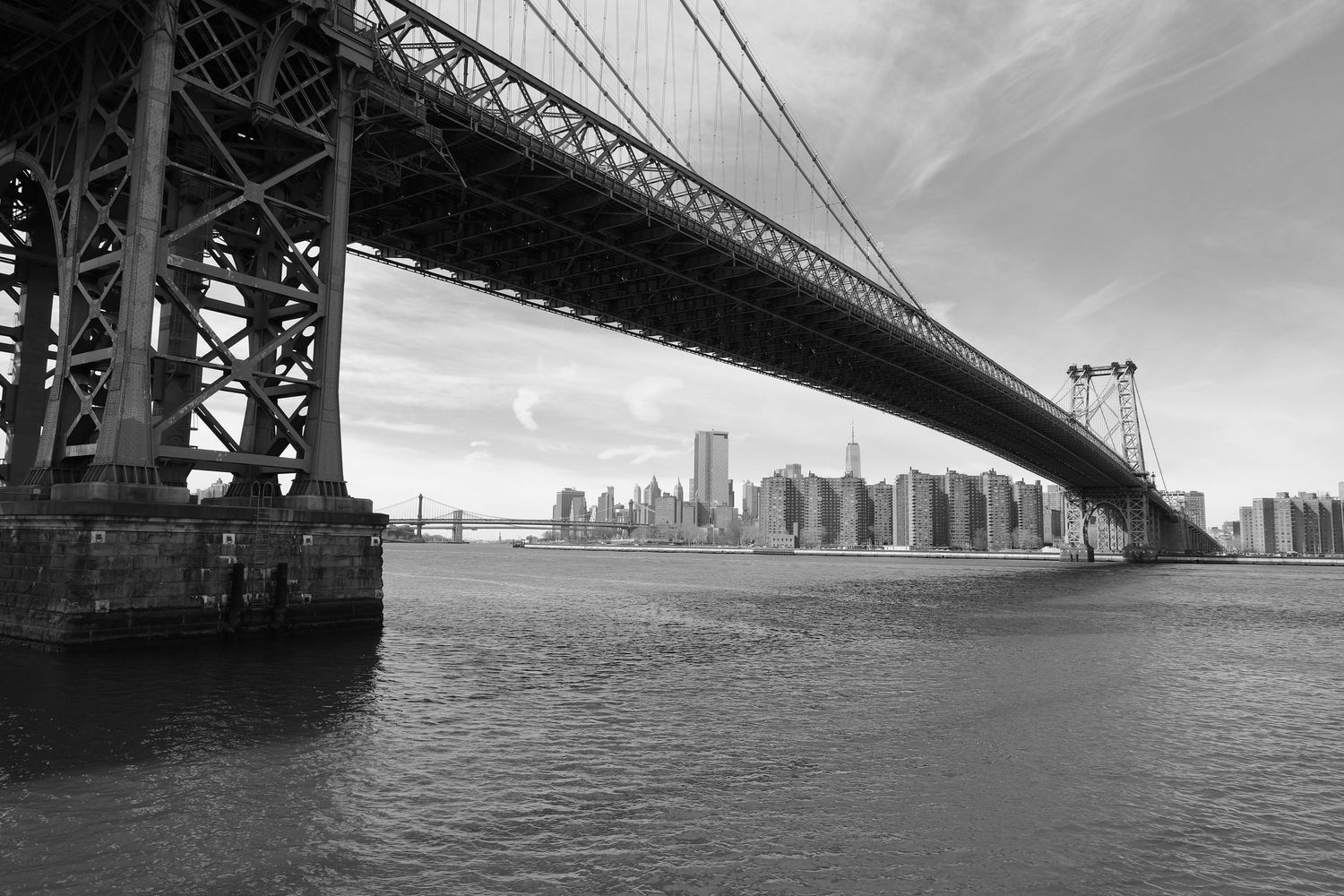 Manhattan skyline and the Manhattan Bridge captured in dramatic black and white from the waterfront.