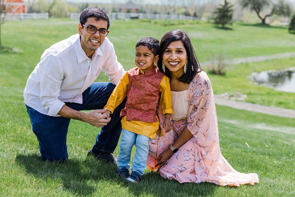 A beautiful family photo taken outdoors on a grassy hill with a pond in the background.