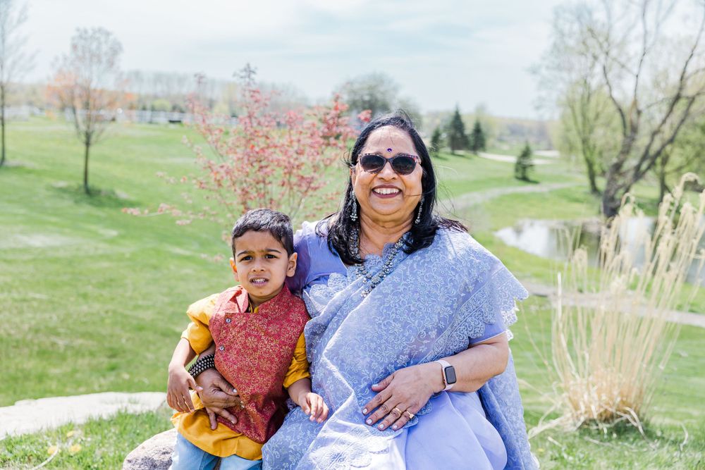 A woman in a blue sari sits outdoors with a child in a casual park setting.