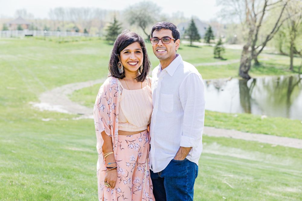 A couple poses outdoors wearing modern South Asian inspired clothing near a pond.