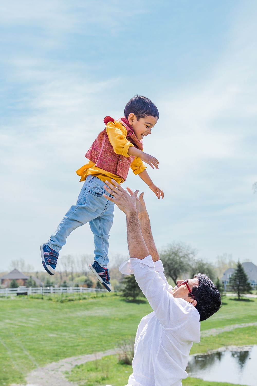 Playful moment captured of parent tossing child in the air against blue sky in park setting.