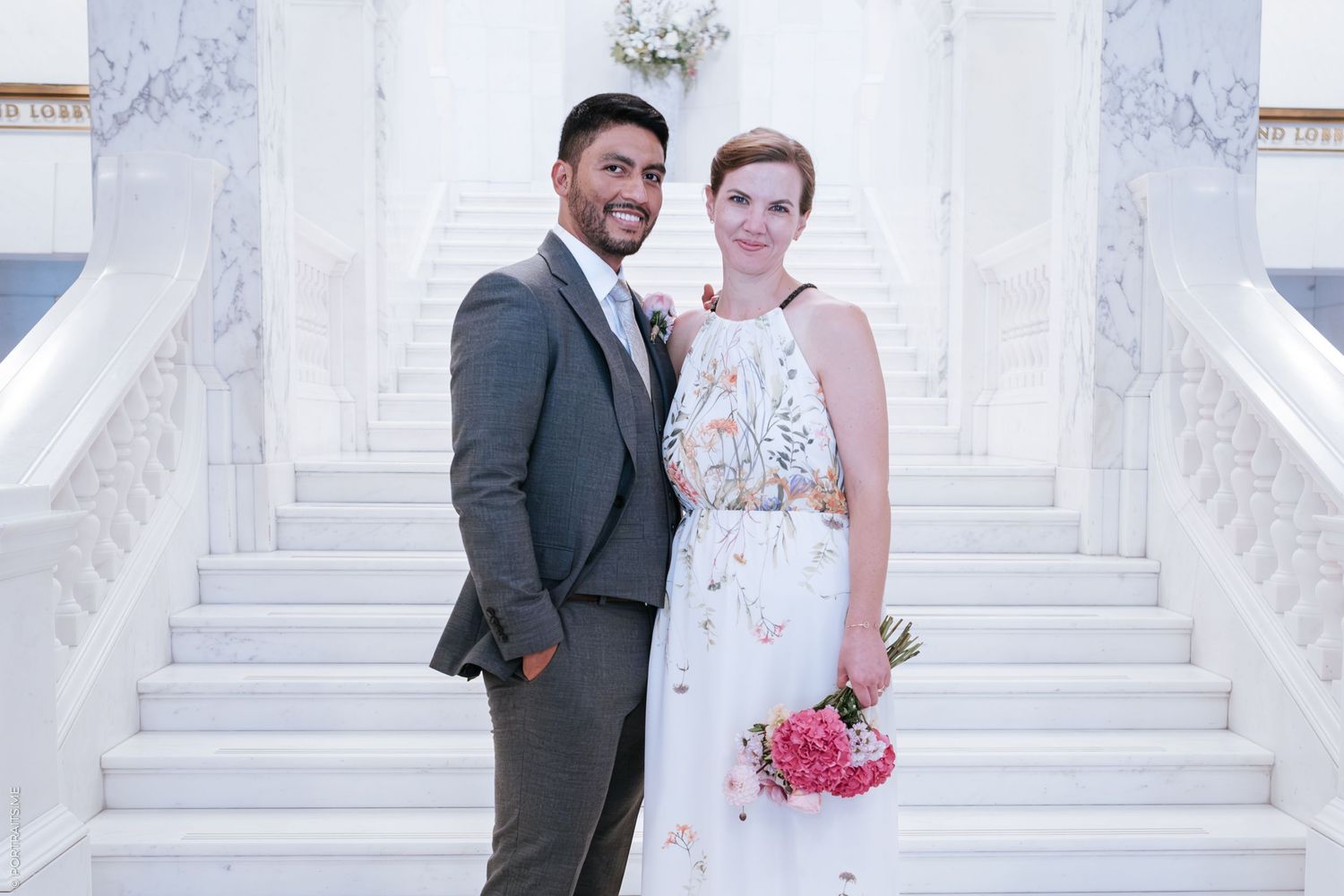 A couple poses for a portrait on white marble steps during their wedding day.