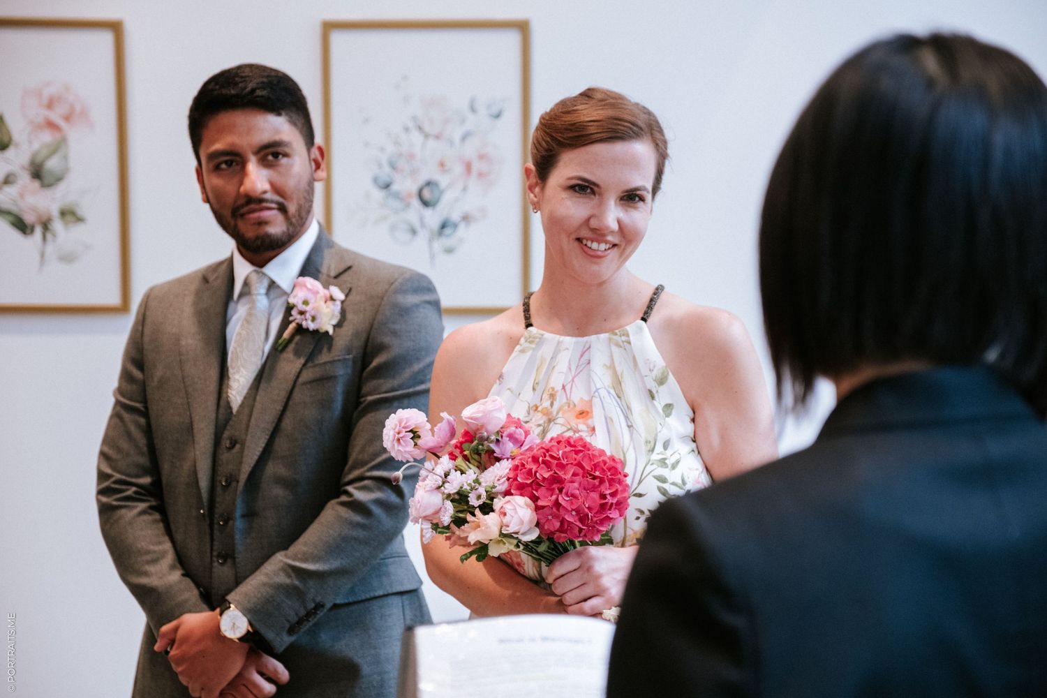 A couple stands at the altar with pink floral decorations during their wedding ceremony.