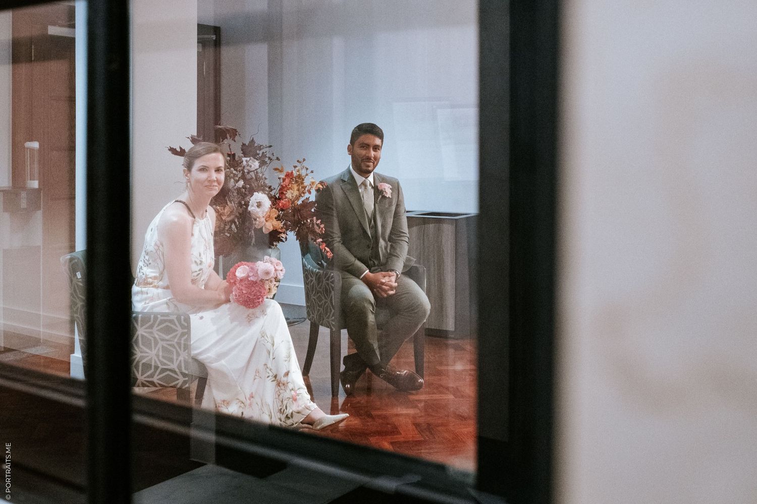 A wedding couple seen through glass sitting together during their ceremony.