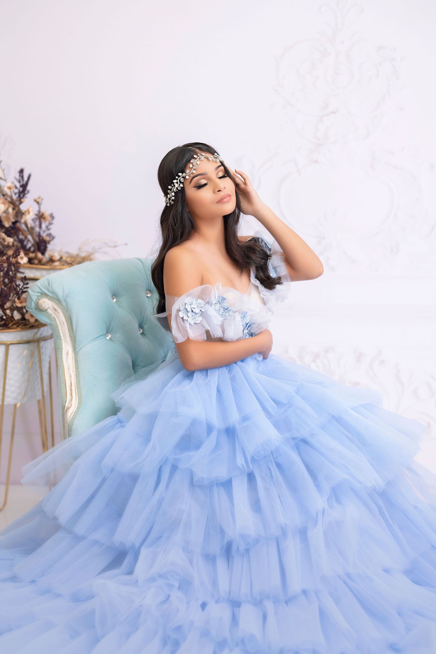 Princess-inspired photo of woman in flowing blue tulle gown and crystal headpiece on tufted chair.