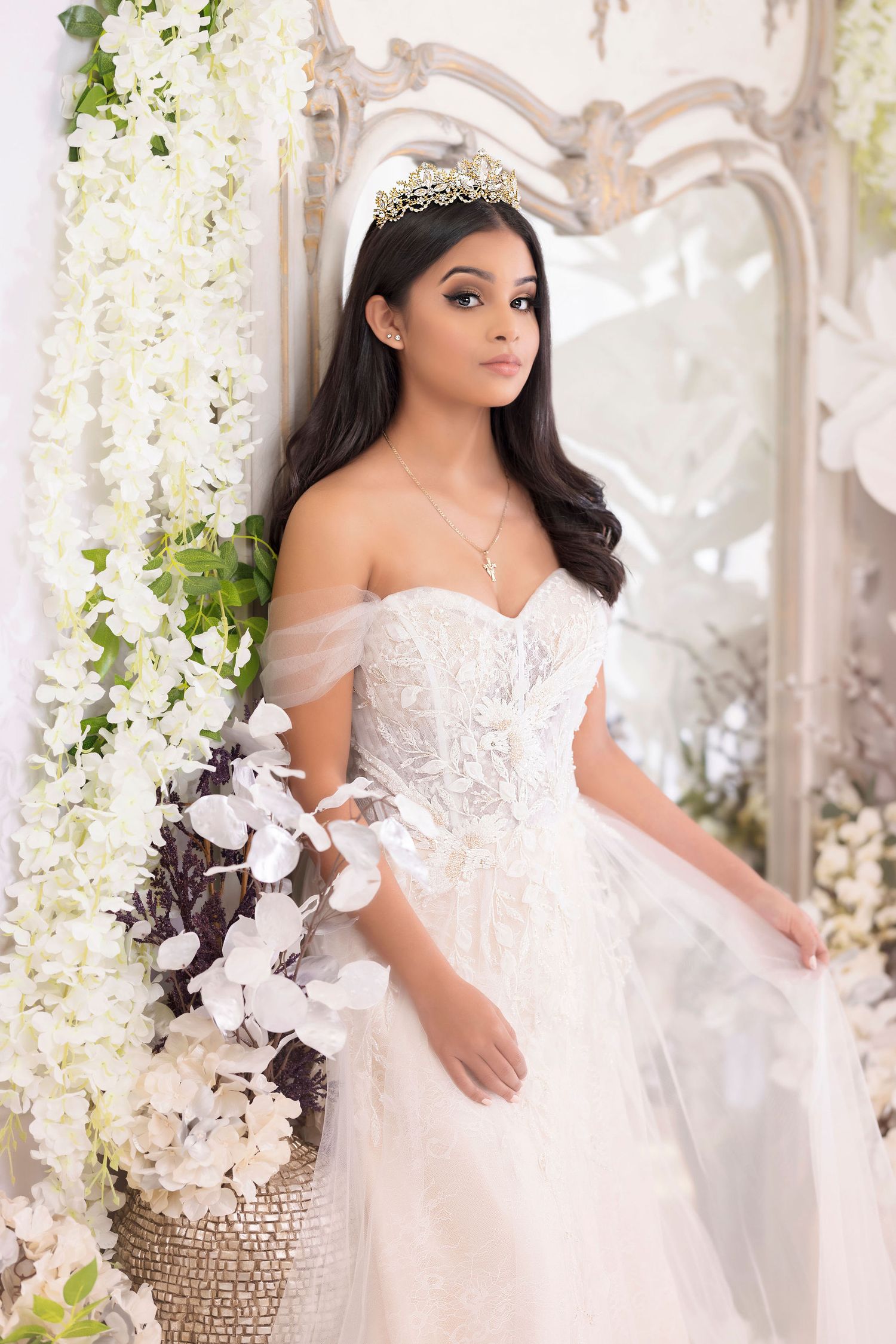 Ethereal bridal portrait with white floral backdrop and off-shoulder lace wedding gown.