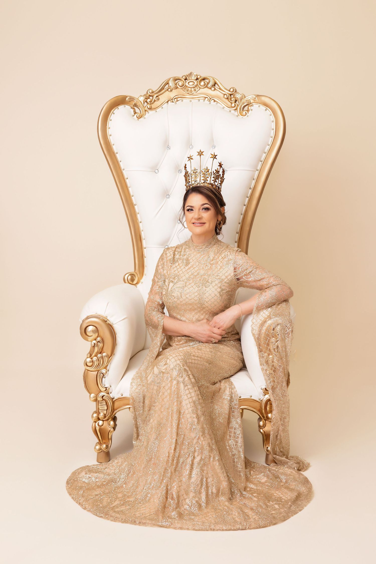 Regal portrait in an ornate gold chair wearing a champagne beaded gown and crown.
