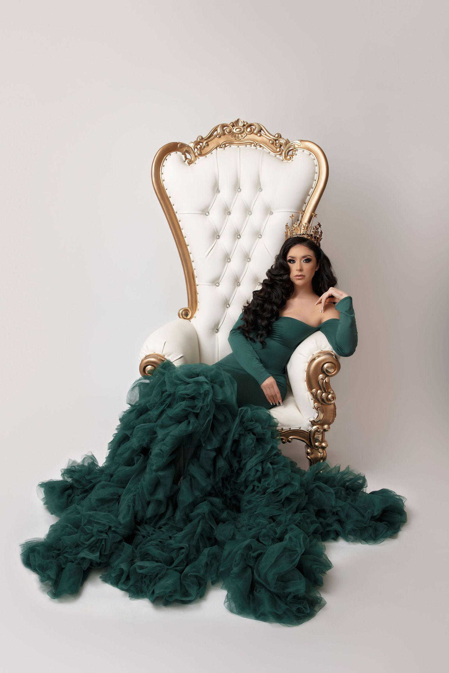 Dramatic emerald gown with ruffled train on ornate white and gold throne chair.
