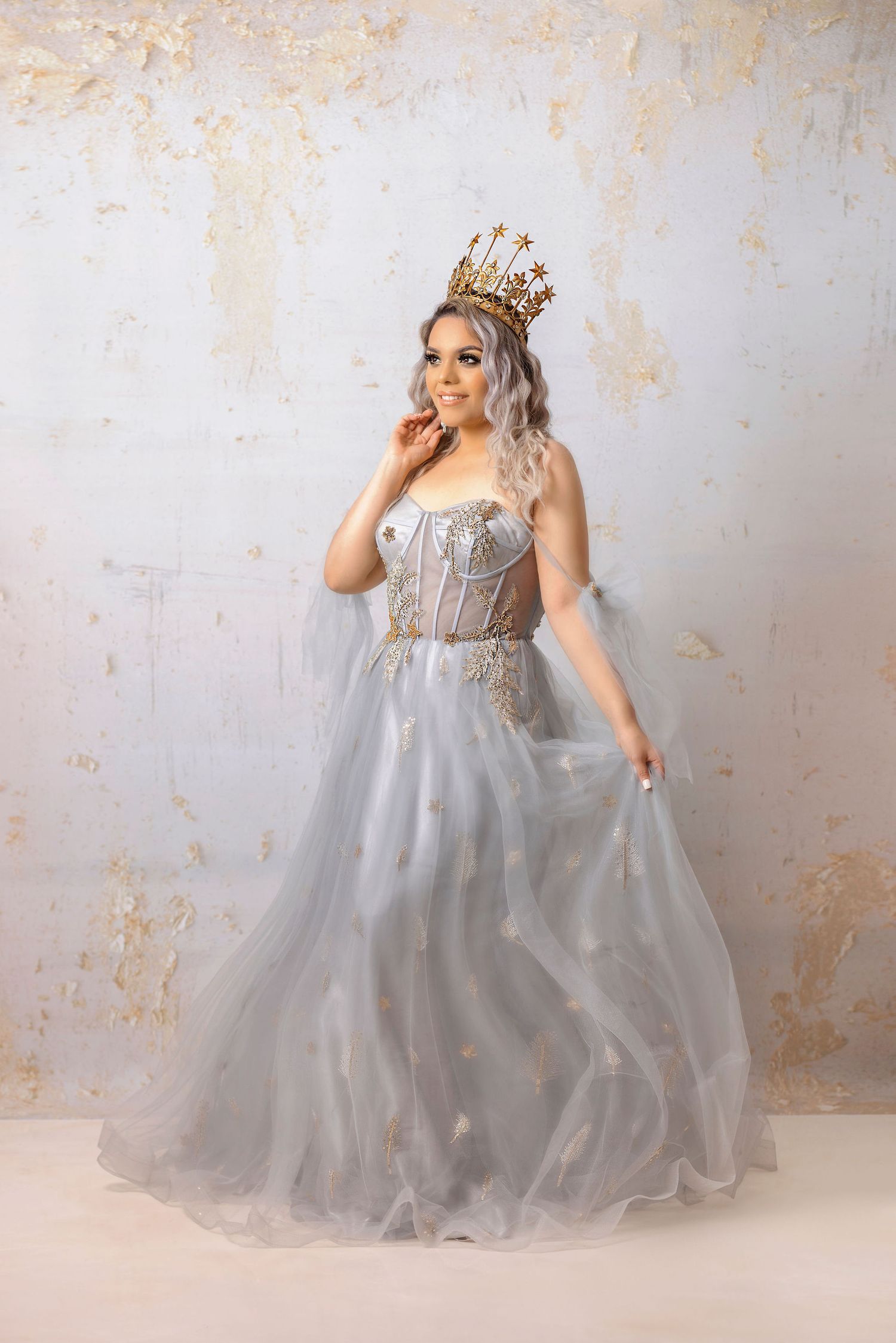 Enchanting silver ballgown with corset detail and golden crown against distressed backdrop.