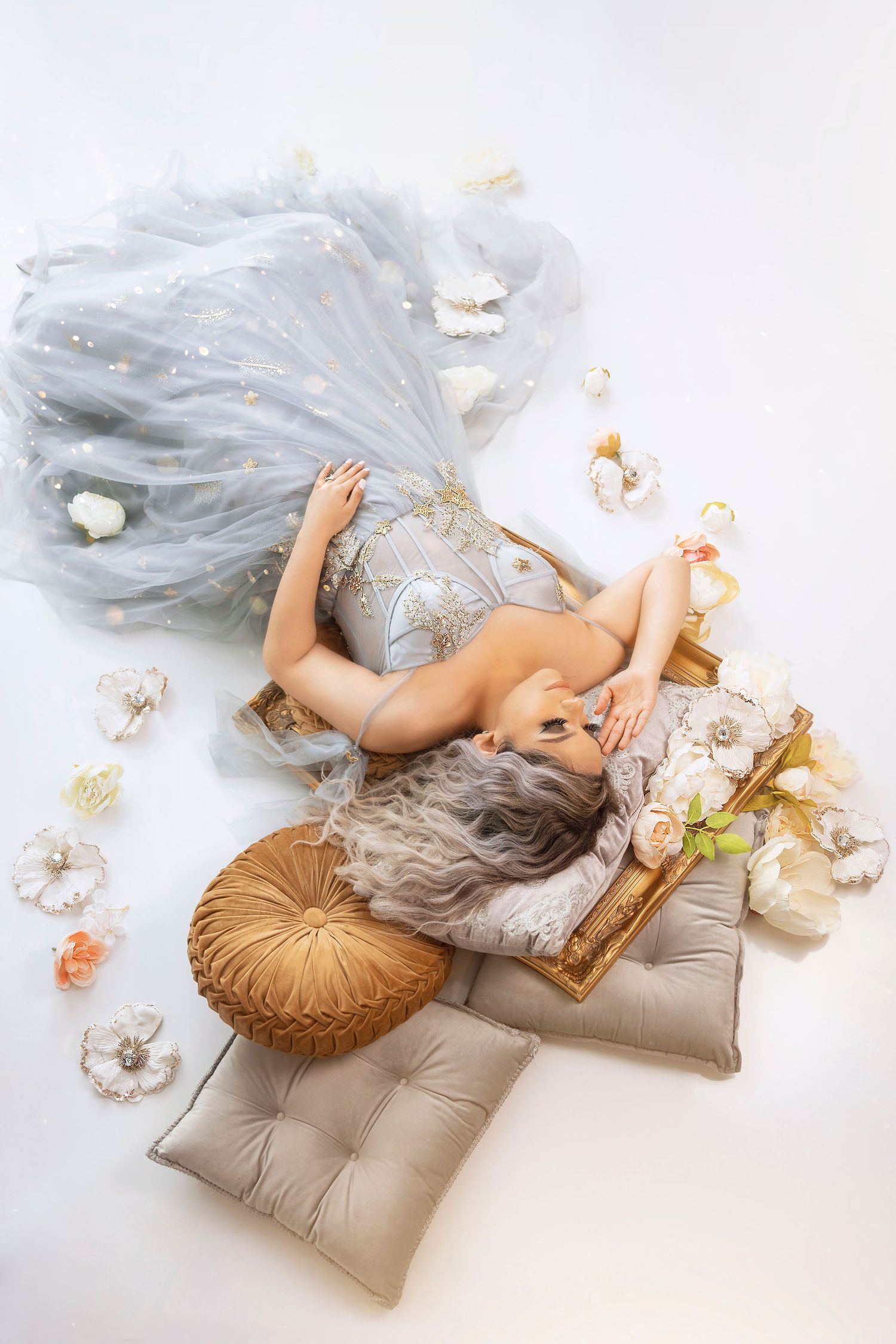 Aerial view of silver tulle gown with scattered flowers and decorative pillows.