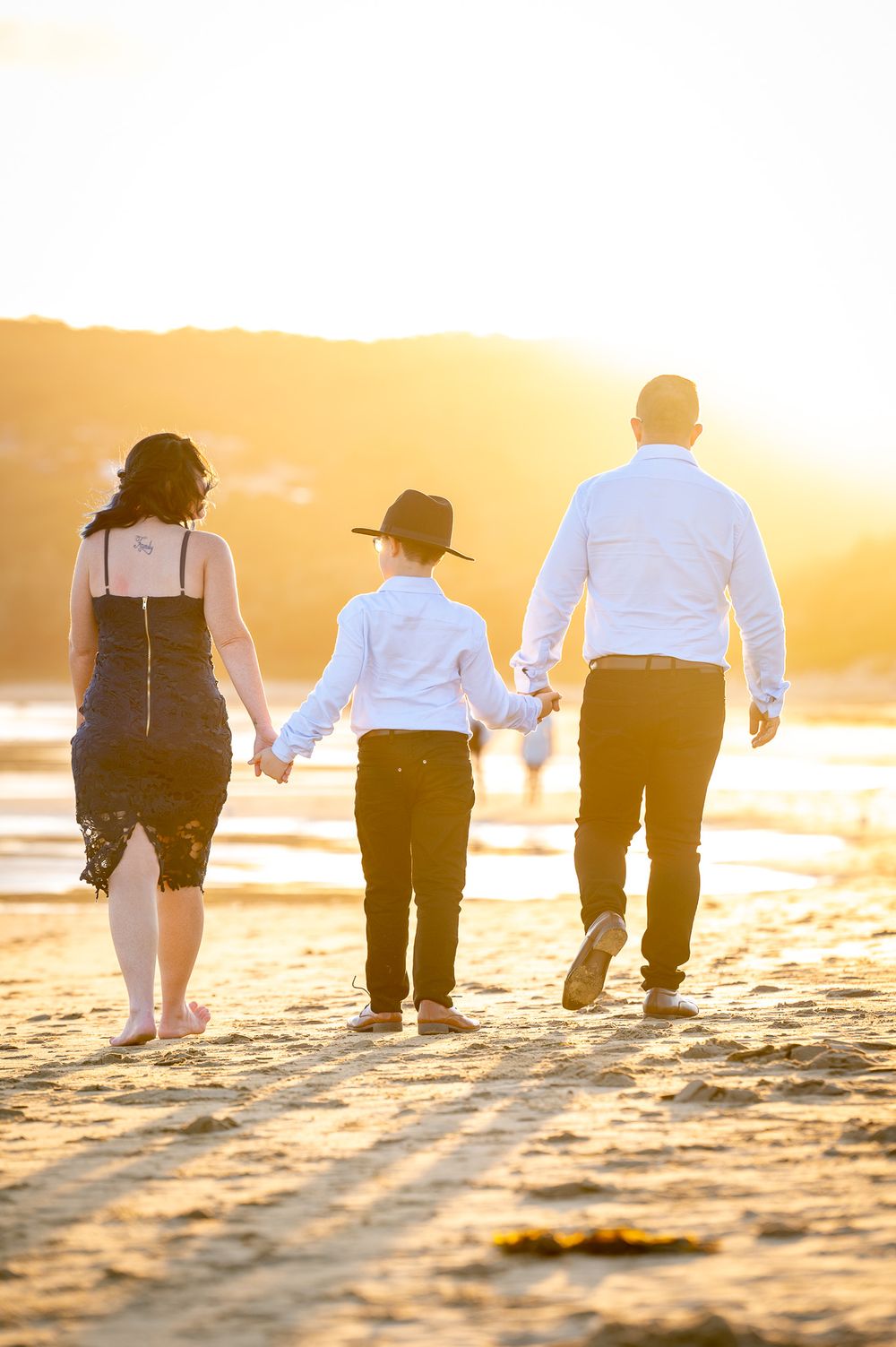 Mum, Dad and Son walking away on the beach at sunset