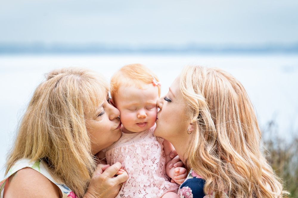 Mum & Nan kissing the Baby in the middle on the cheek