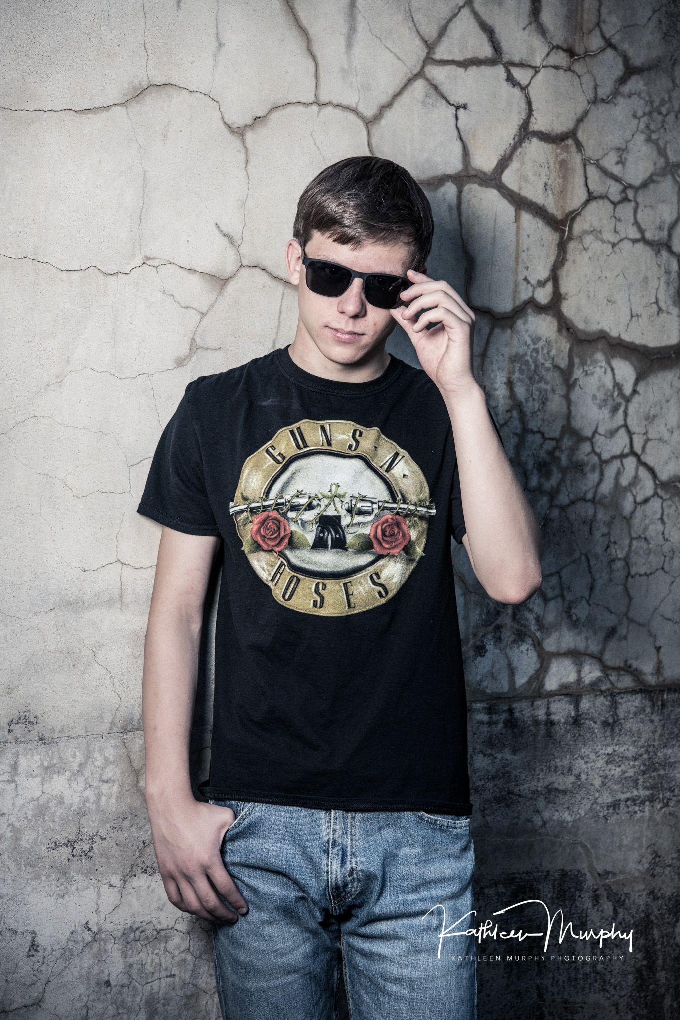 Person wearing Guns N' Roses t-shirt and sunglasses posing against textured concrete wall.