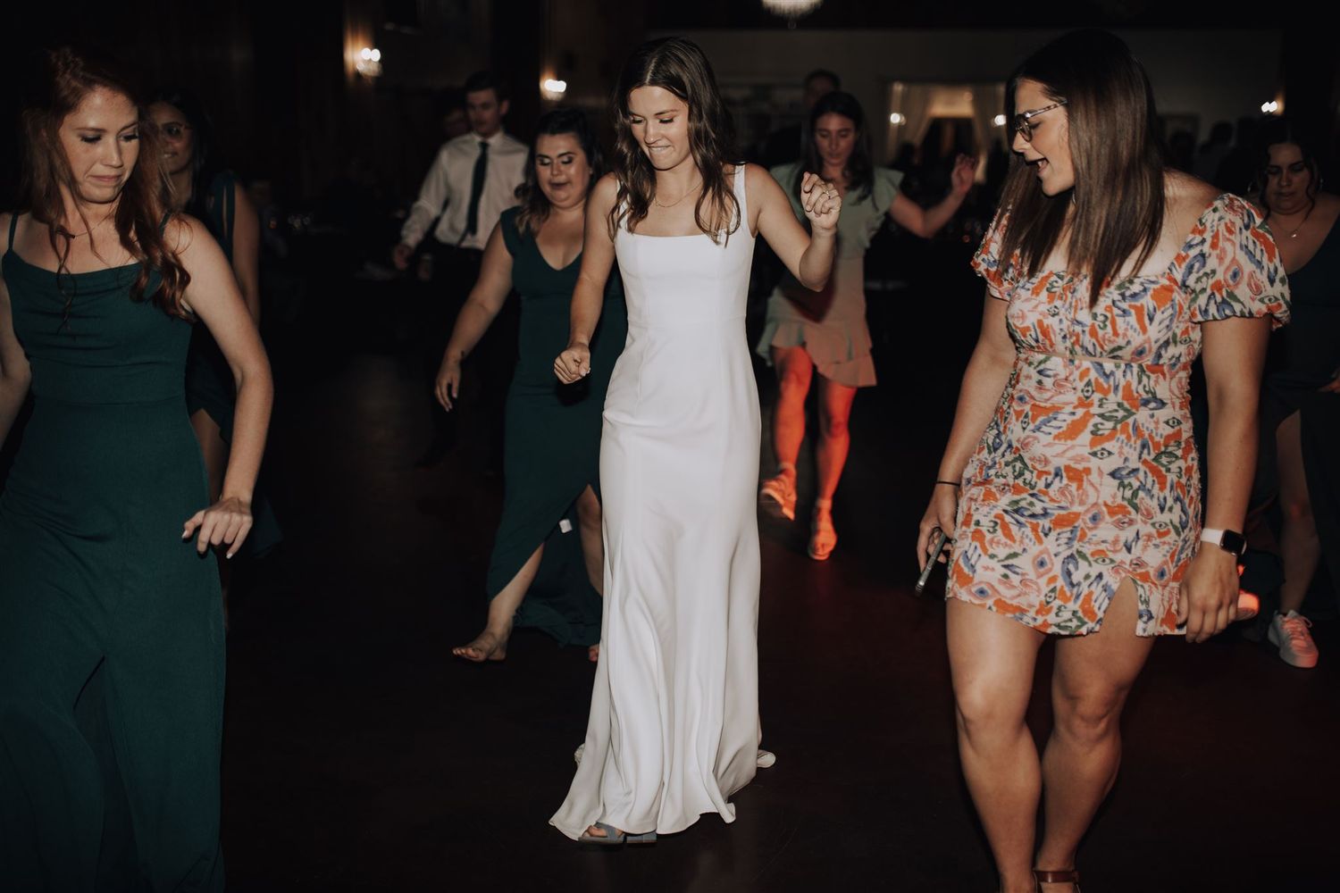 Wedding party dancing together in elegant dresses on a dark dance floor.