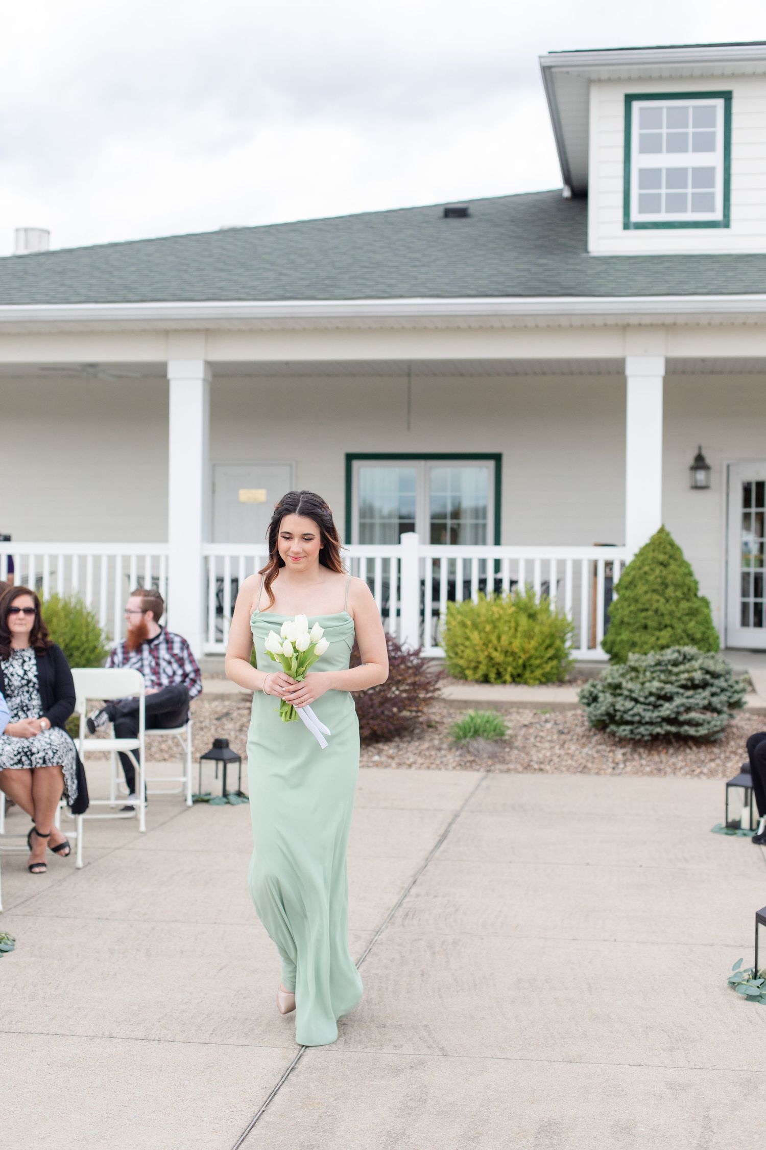 A person in a mint green dress poses gracefully on a porch with white columns and railing.