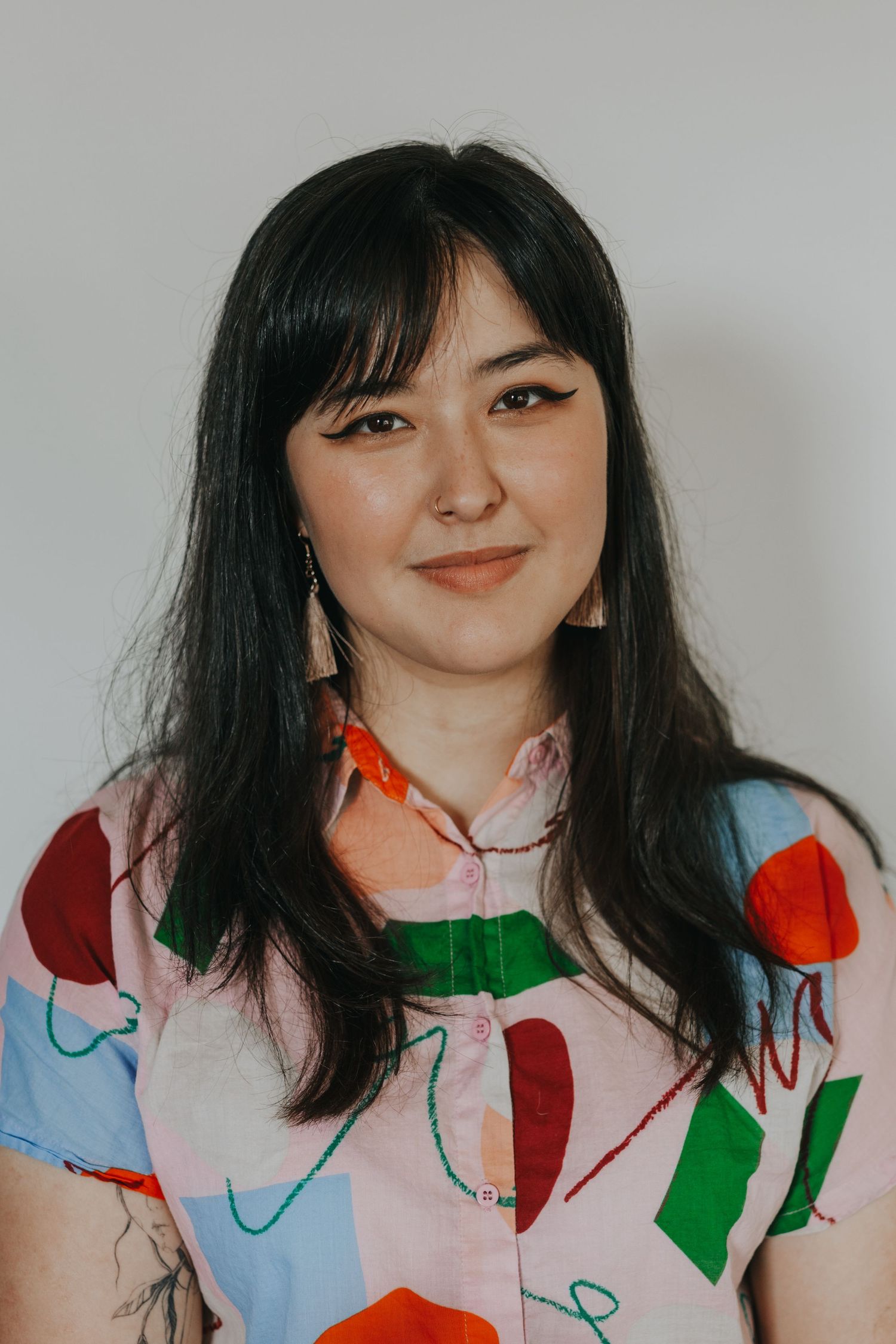 Professional portrait of a woman wearing a colorful patterned shirt against a light background.