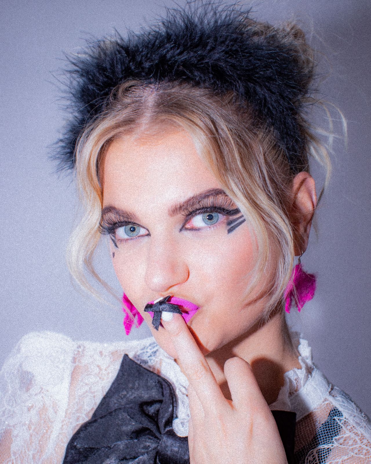 Fashion portrait with dramatic makeup, pink lipstick, and spiky black hairstyle against a grey background.