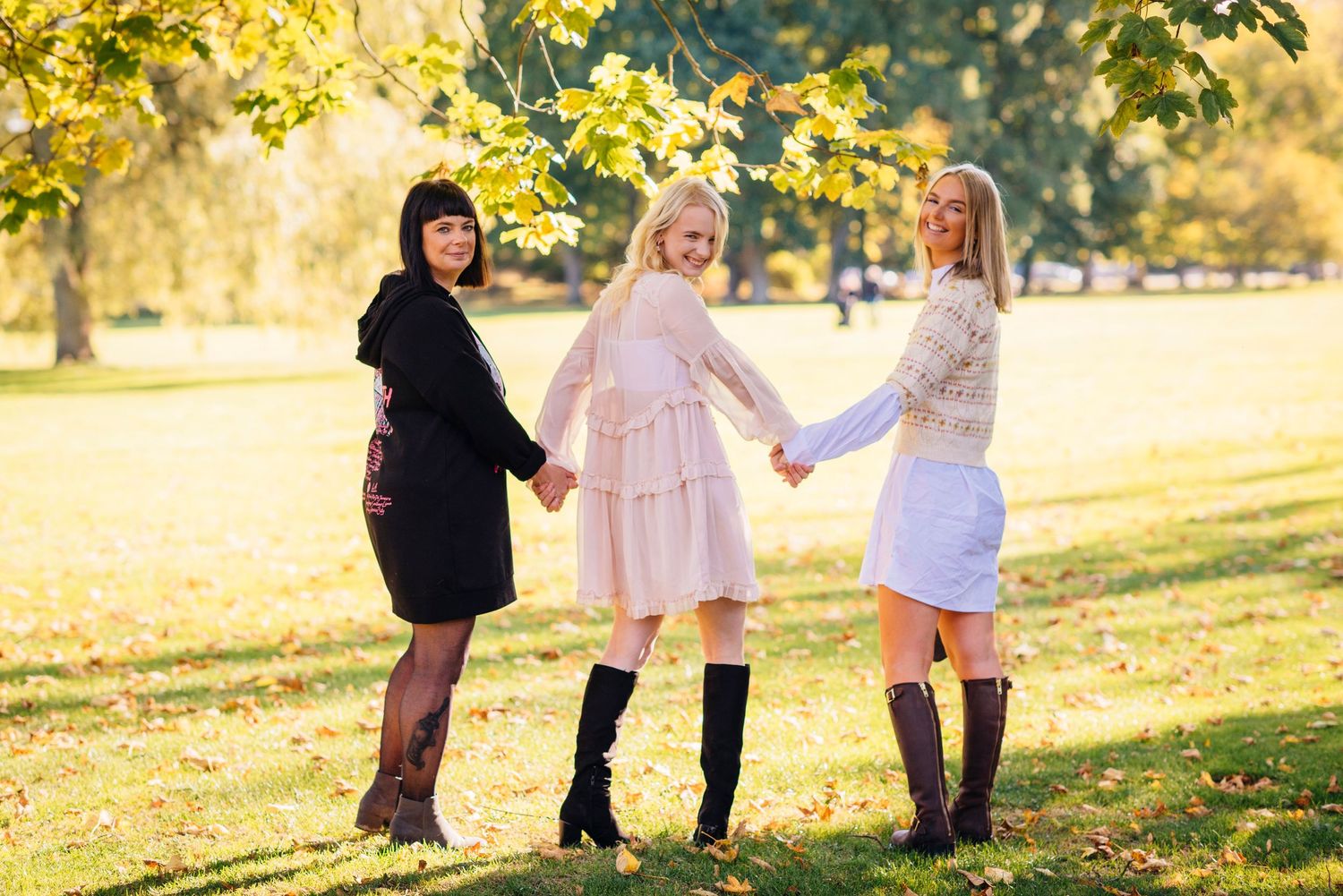 Mother and daughters holding hands and walking together through a sunlit autumn park with golden leaves falling.