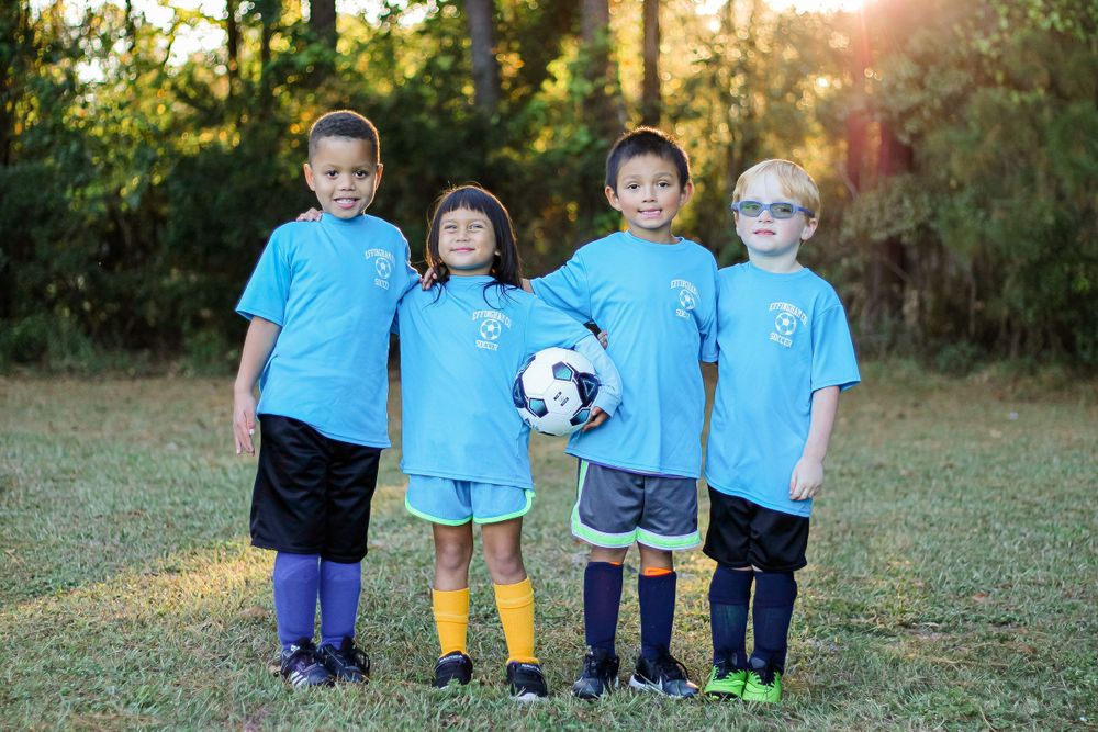 Four young soccer players in matching light blue uniforms stand together holding a ball.