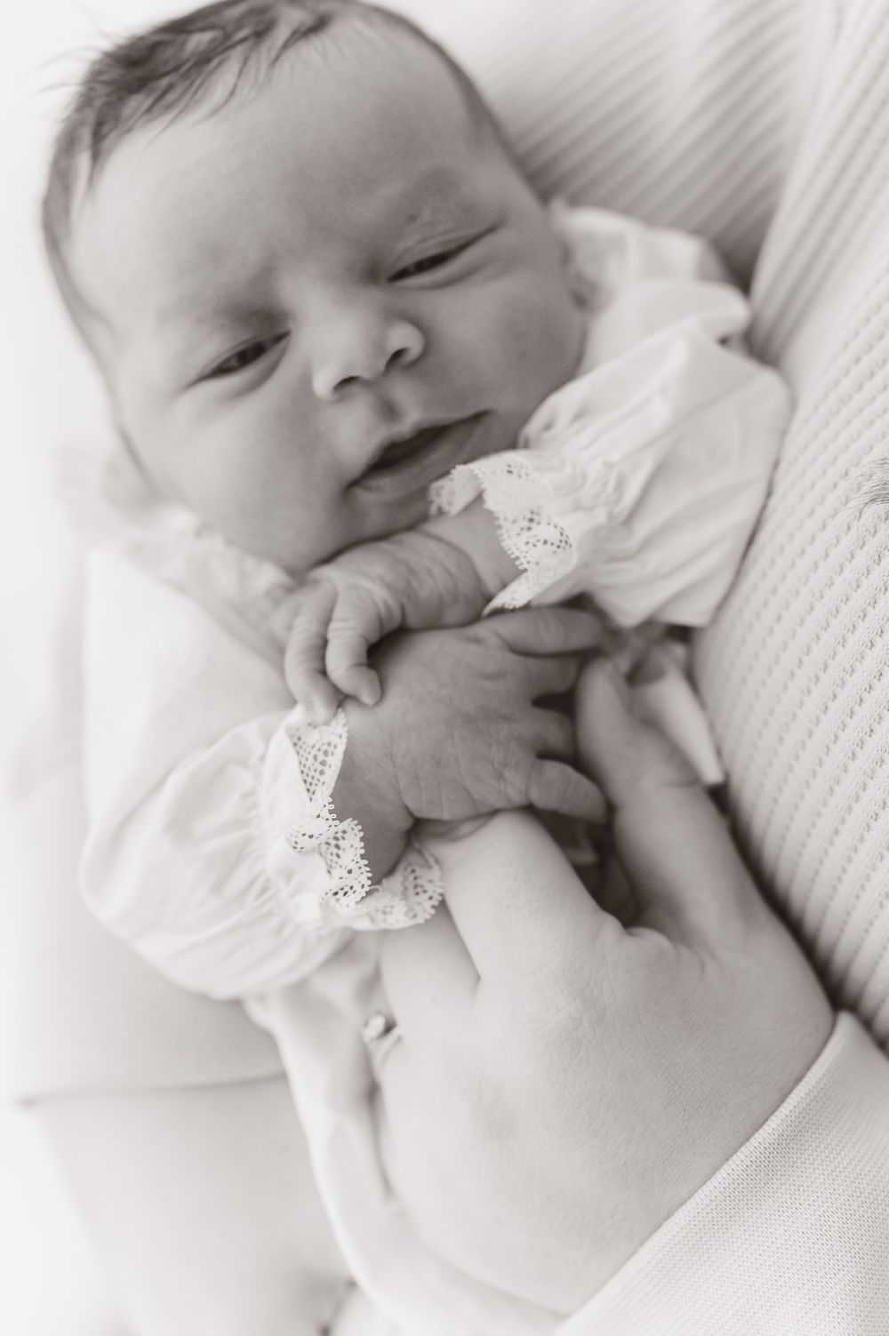 Close-up black and white portraits of sleeping newborn in delicate white lace outfit.