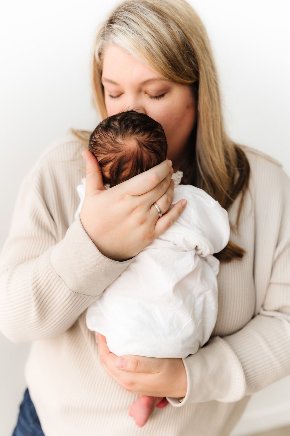 A tender moment captured in a series of intimate photos showing a parent cradling a newborn in a cream sweater.