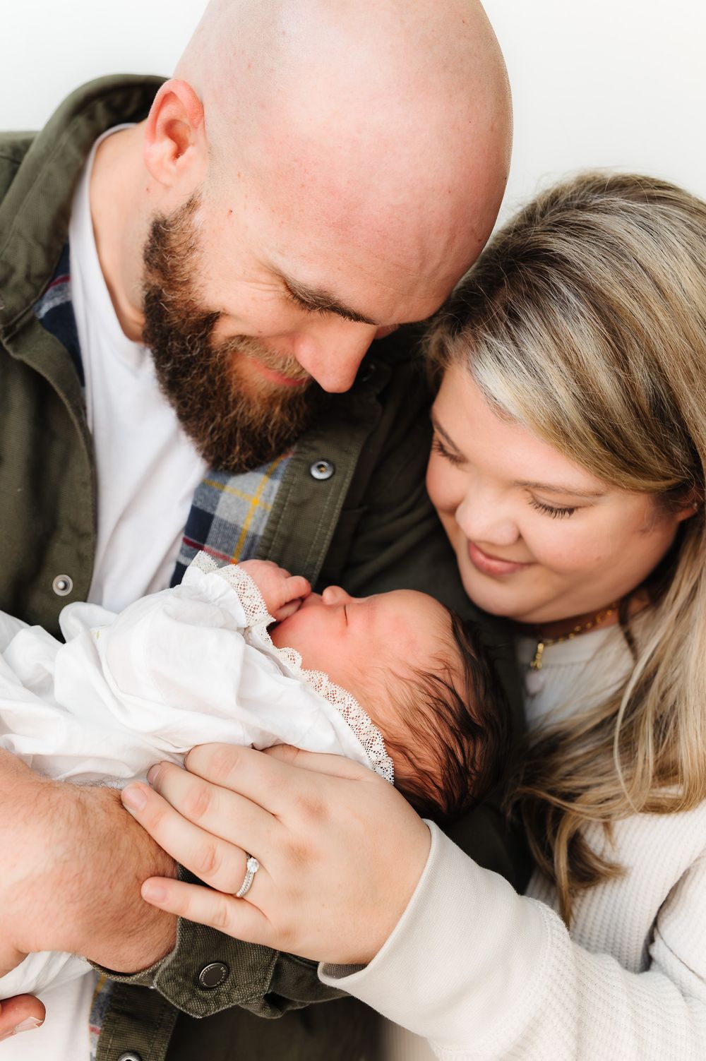 Intimate family photos showing parents sharing loving moments with their newborn baby against a white background.