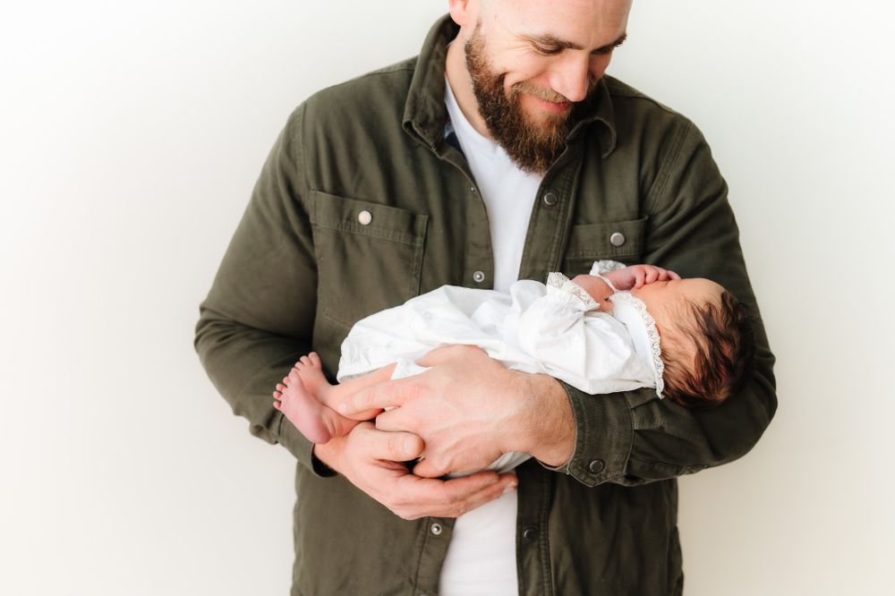 Parent in olive jacket holding sleeping newborn baby against white background.