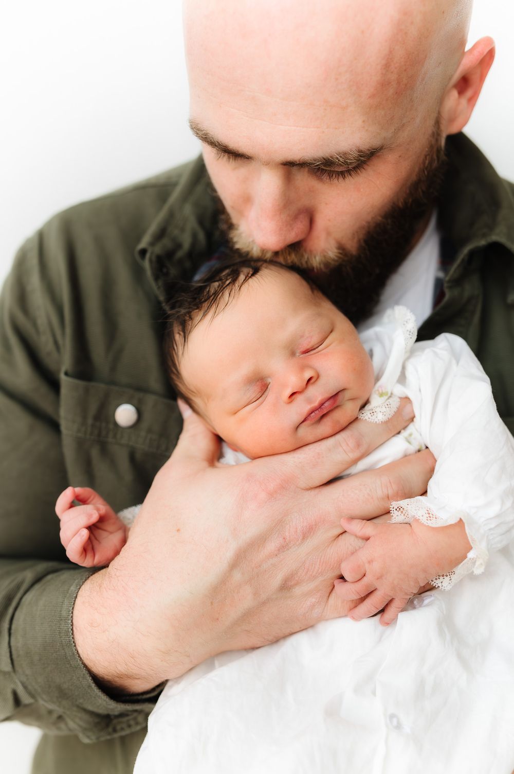 Tender close-up shots of parent kissing newborn baby wrapped in white.