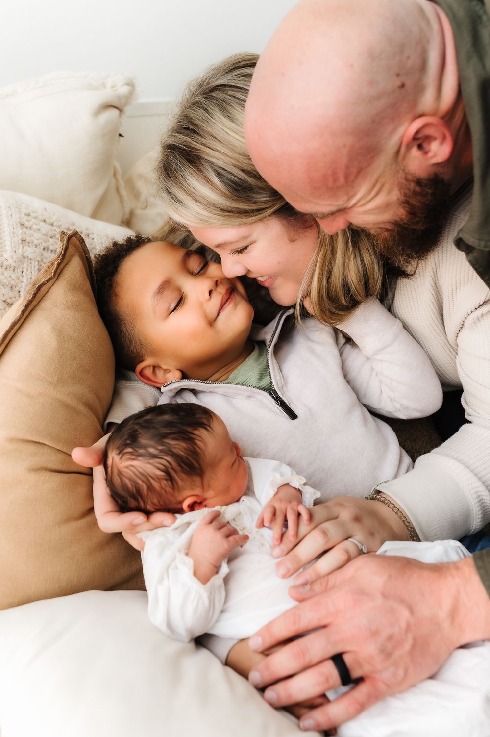 Family cuddle moment with newborn baby on cream colored bedding.