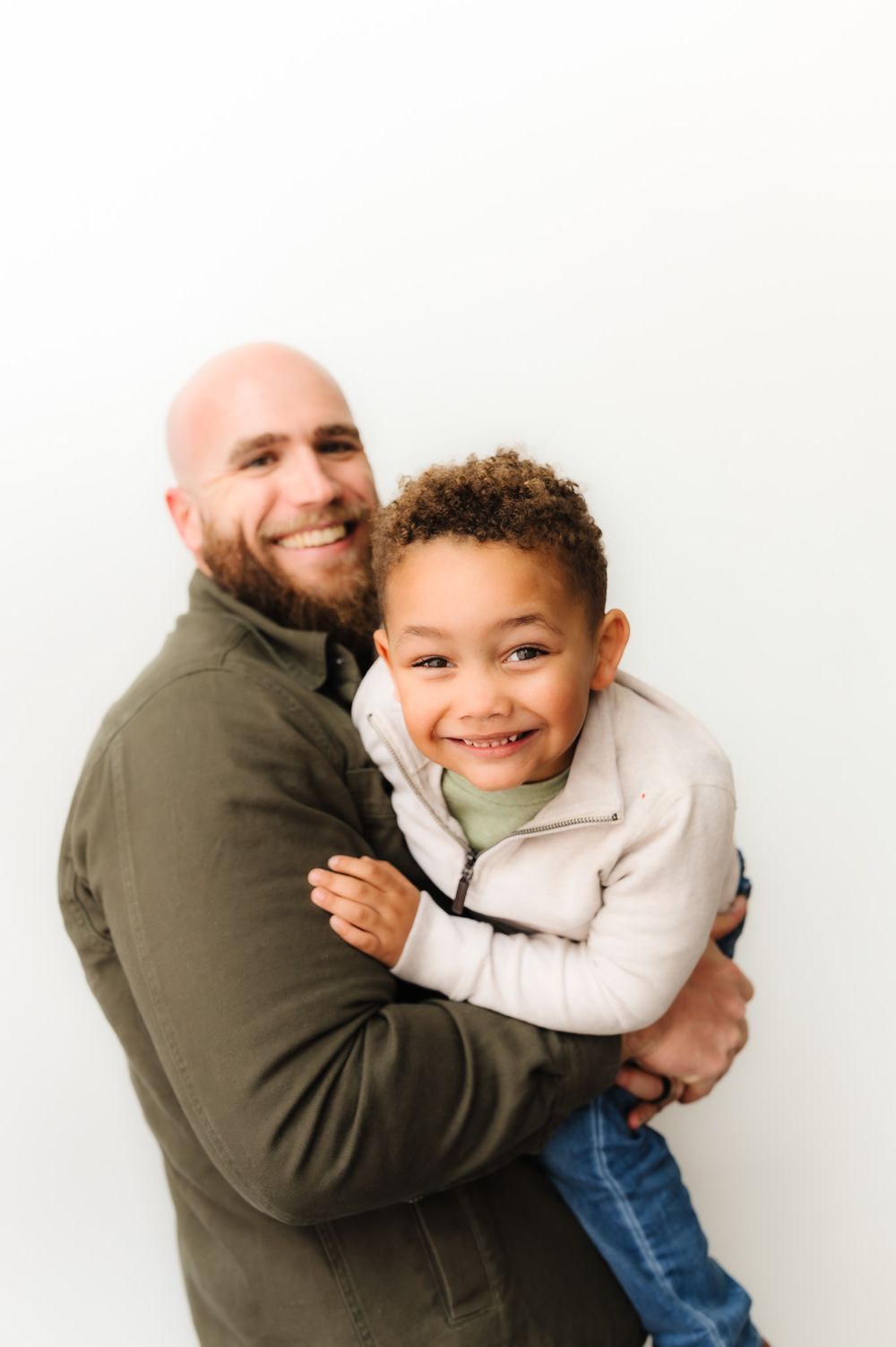 Playful father-son portrait session against white background showing joyful interaction.