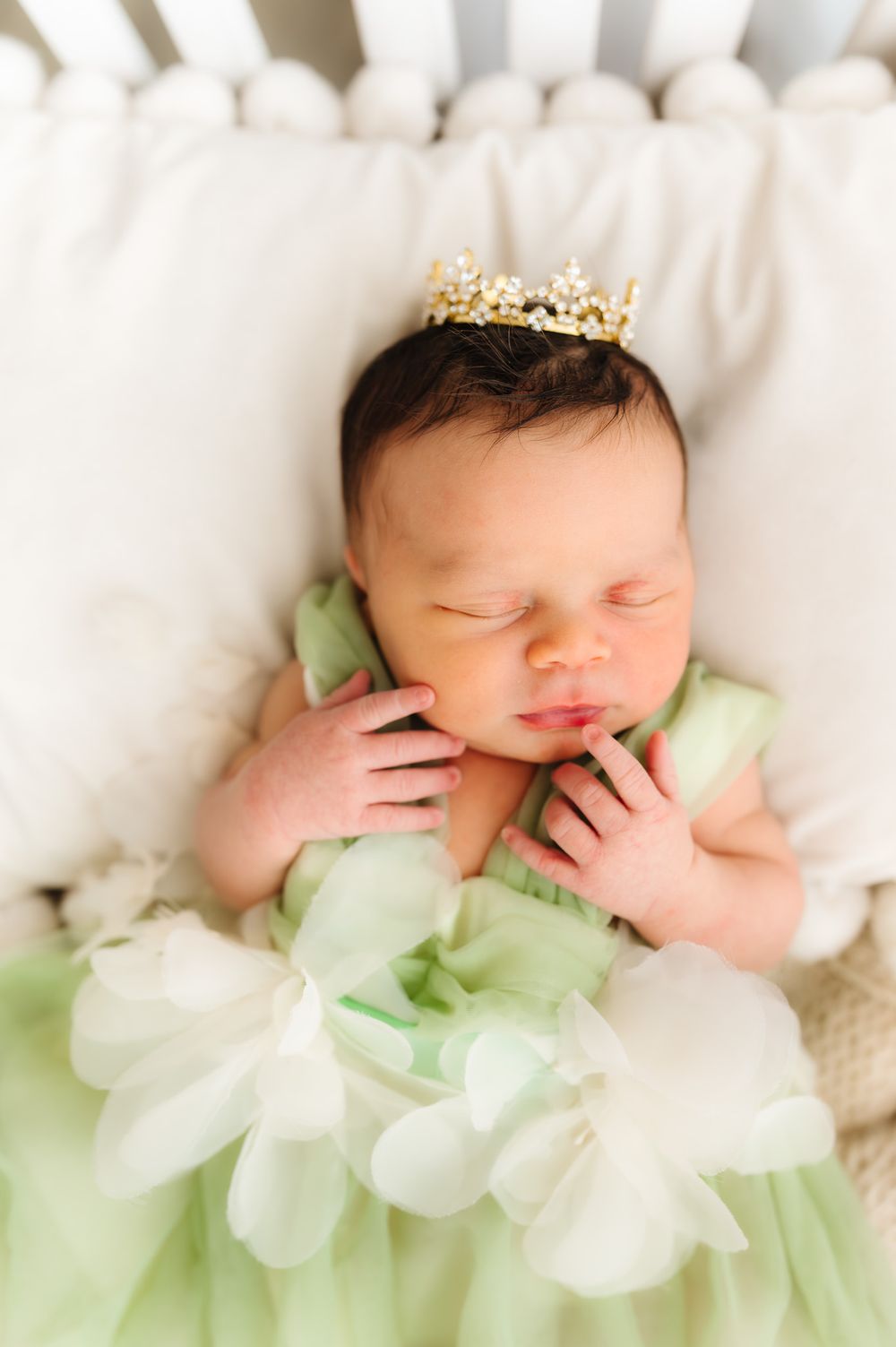Sleeping newborn in mint green outfit wearing tiny crown during portrait session.