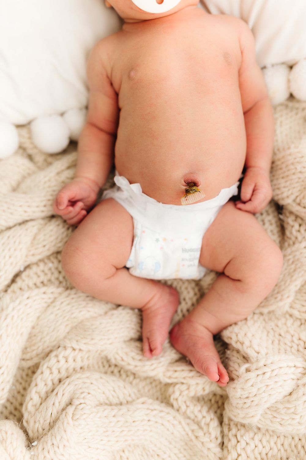Newborn baby wearing white diaper lying on textured cream blanket.