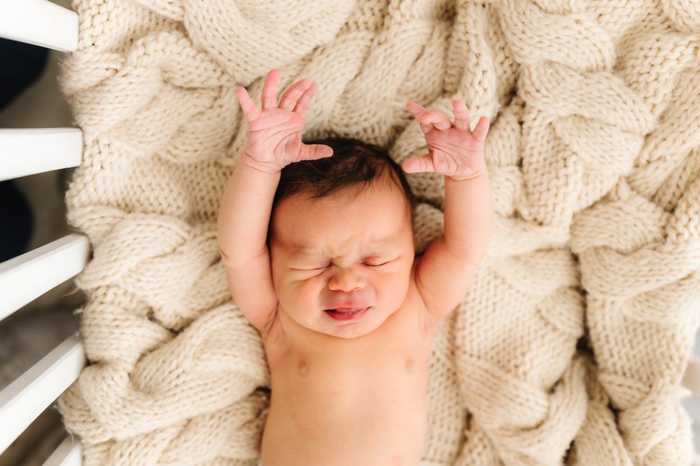 Newborn baby stretching on cream cable knit blanket during photo session.
