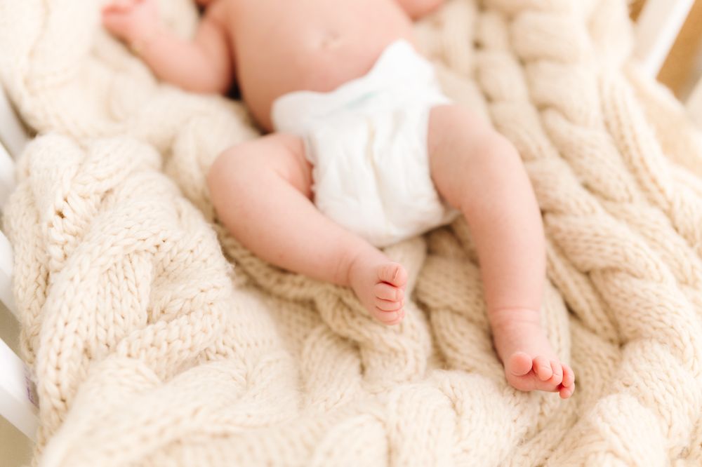 Close-up details of tiny baby feet and limbs on a cream knit blanket.