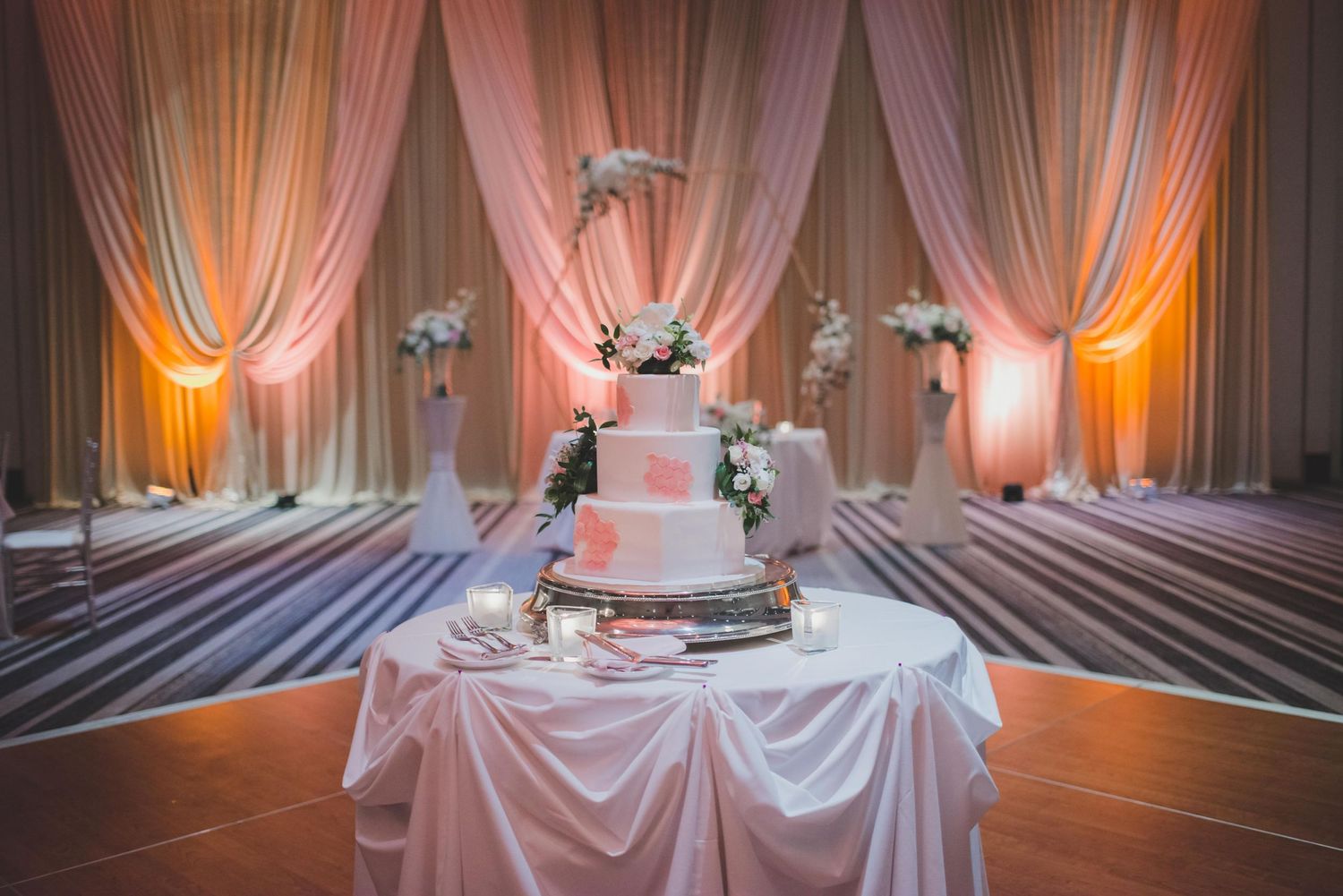 Wedding reception room with pink uplighting, draped fabric walls, and elegant table settings.
