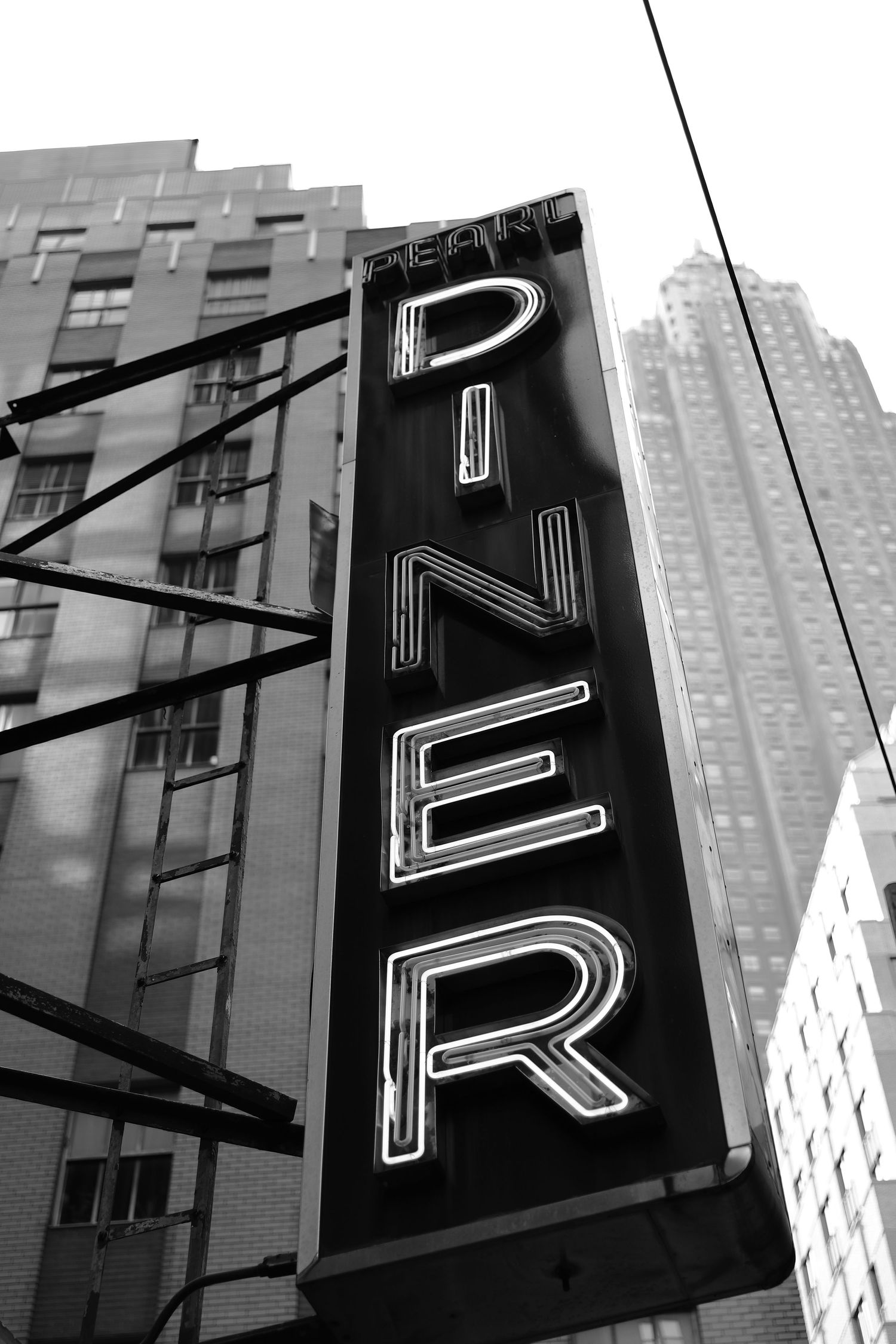 Vintage black and white neon diner sign mounted on city building with skyscrapers in background.