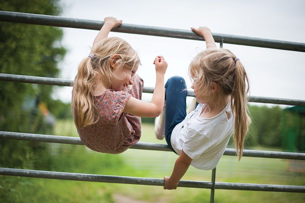 Two children play and hang upside down on outdoor playground bars.