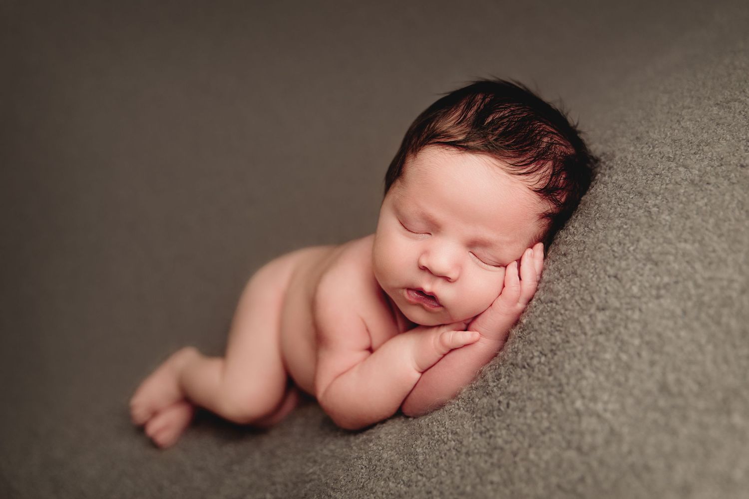 infant boy laying on his side on soft grey blanket hands under his cheek