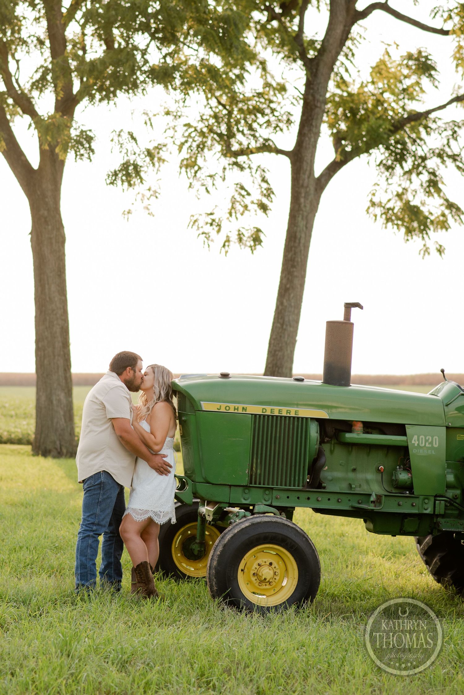 Romantic couple embracing by vintage green John Deere tractor at sunset.
