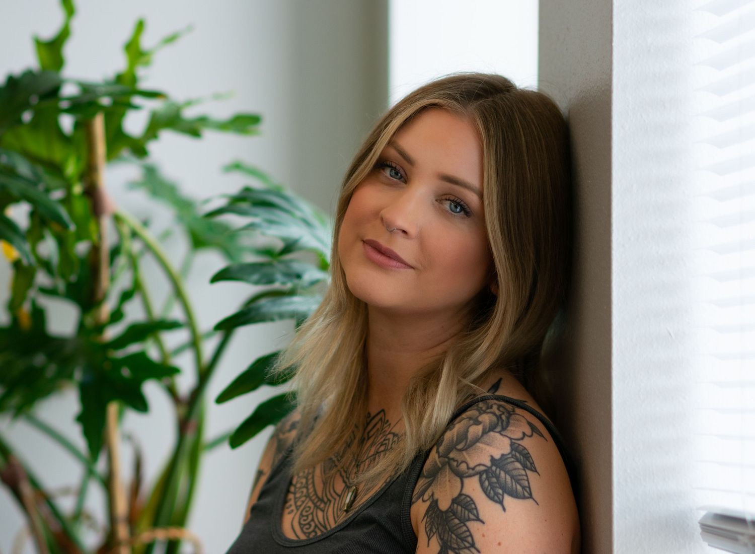 beautiful tattooed woman leaning head against wall and looking at camera.