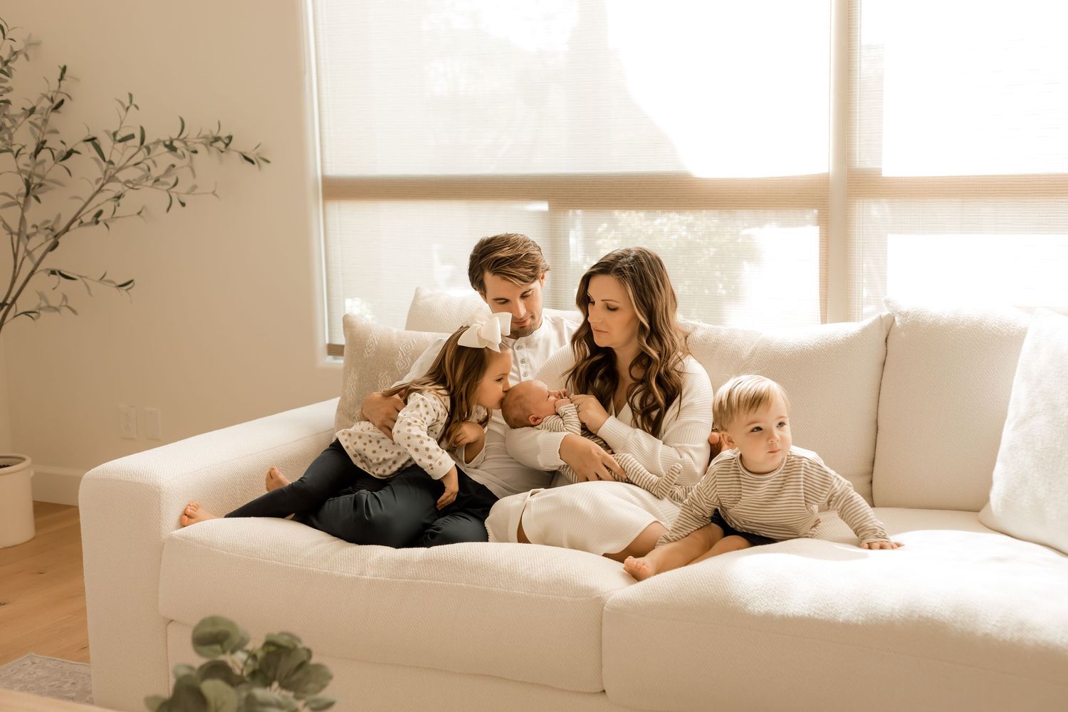 Family snuggling kissing and looking at their newborn baby in the comfort of their own home for their lifestyle newborn session.