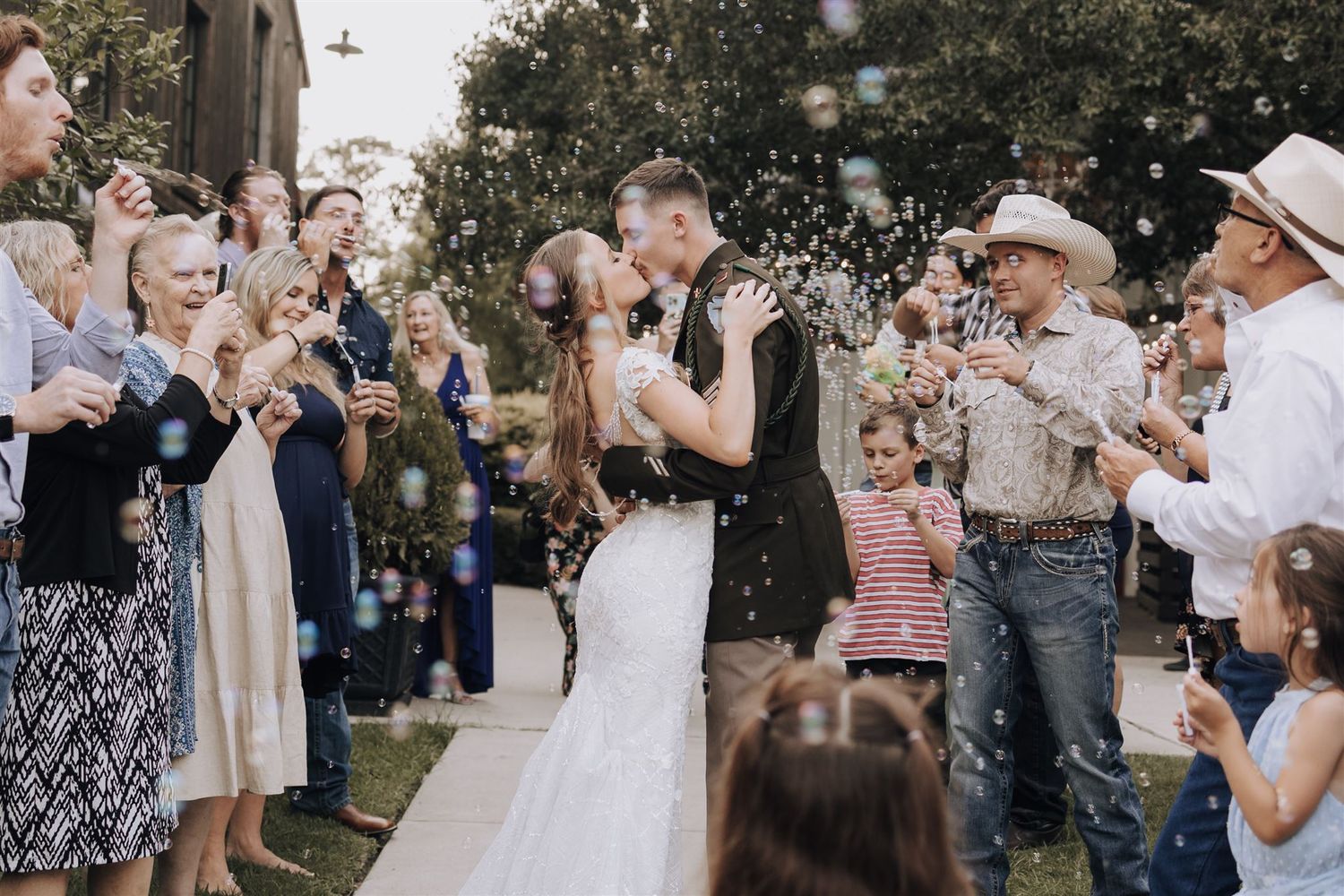 Wedding celebration in outdoor garden setting with guests blowing bubbles.
